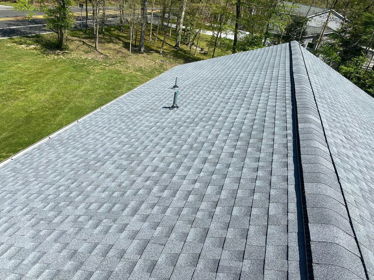 Overhead view of a gray shingled roof on a house with two vents and a tree-lined backyard.