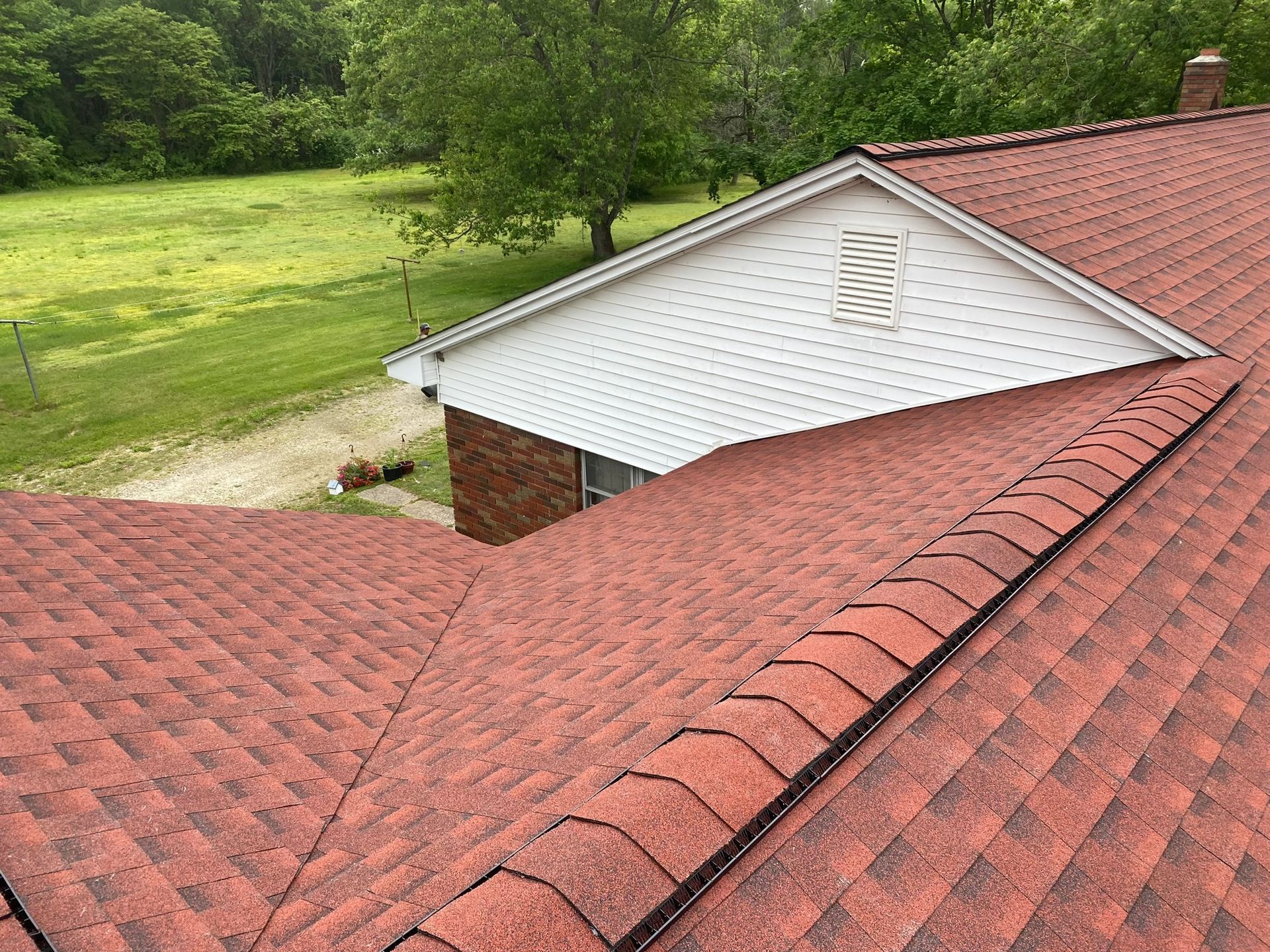 Red shingled roof with a white gable against a green field.