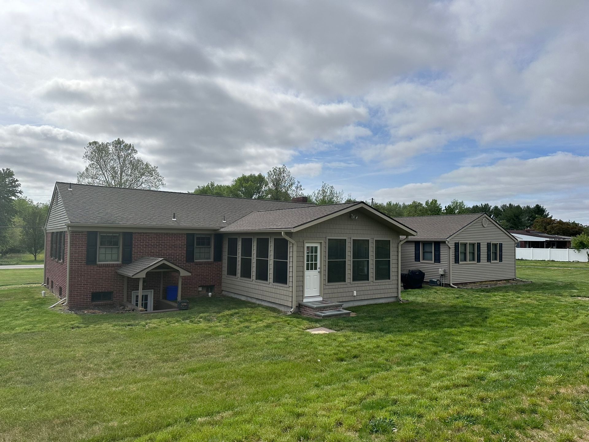 A brick home with a sunroom and detached shed on a grassy lawn under a cloudy sky.