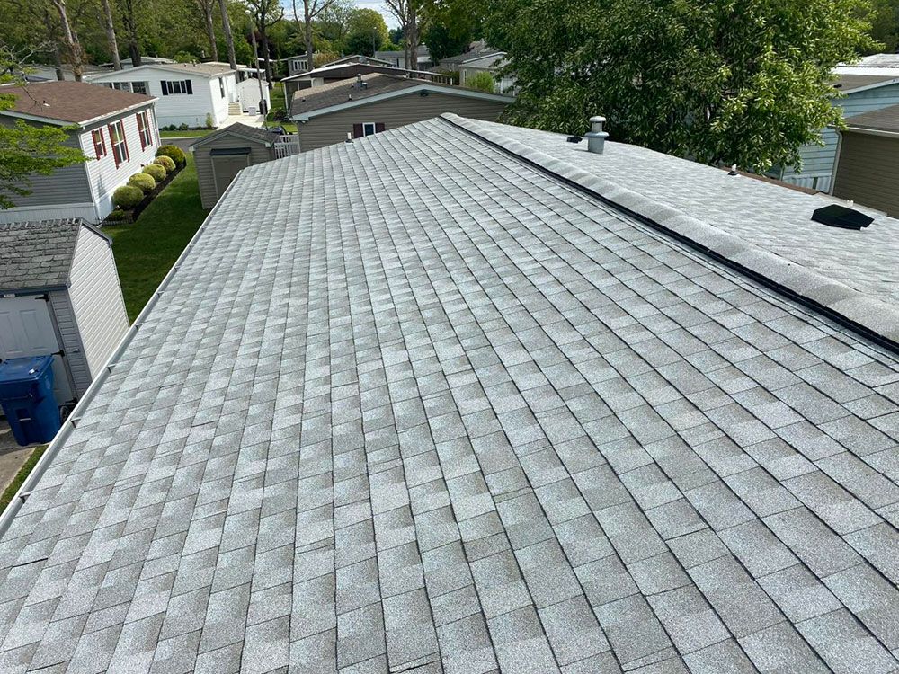 Gray shingled roof on a house, angled shot, with surrounding trees and other buildings.