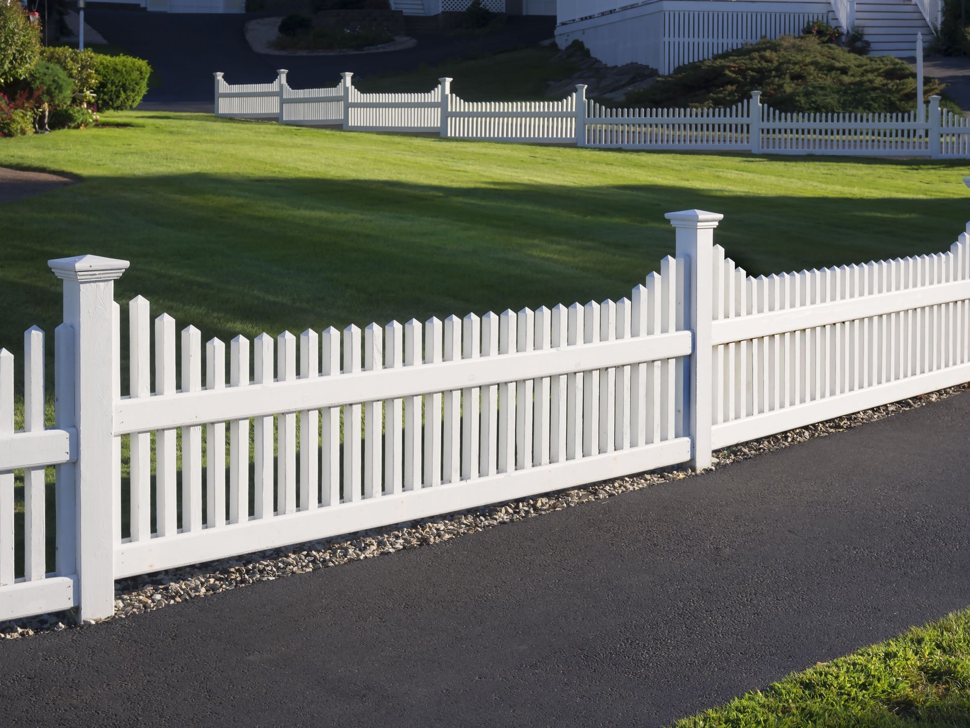 White picket fence bordering a green lawn and paved driveway.