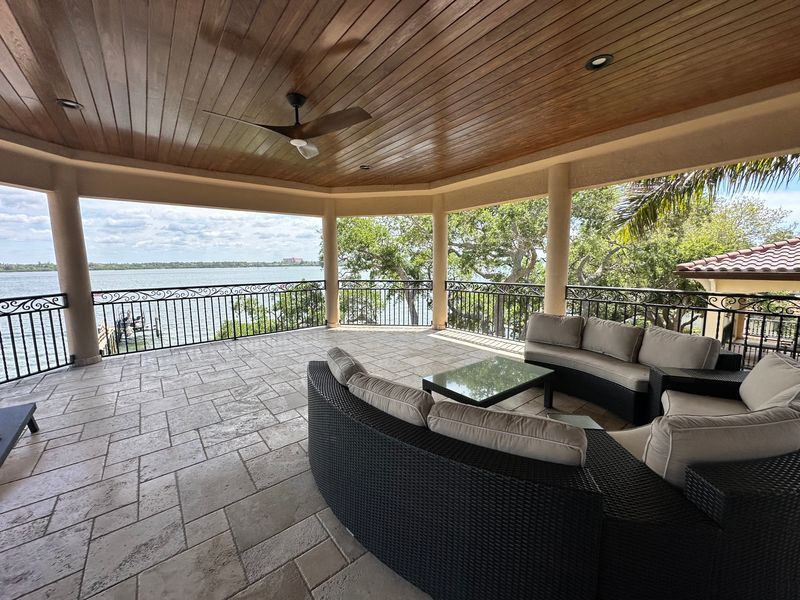 Covered waterfront patio with wicker seating, tiled floor, and open view of the water.