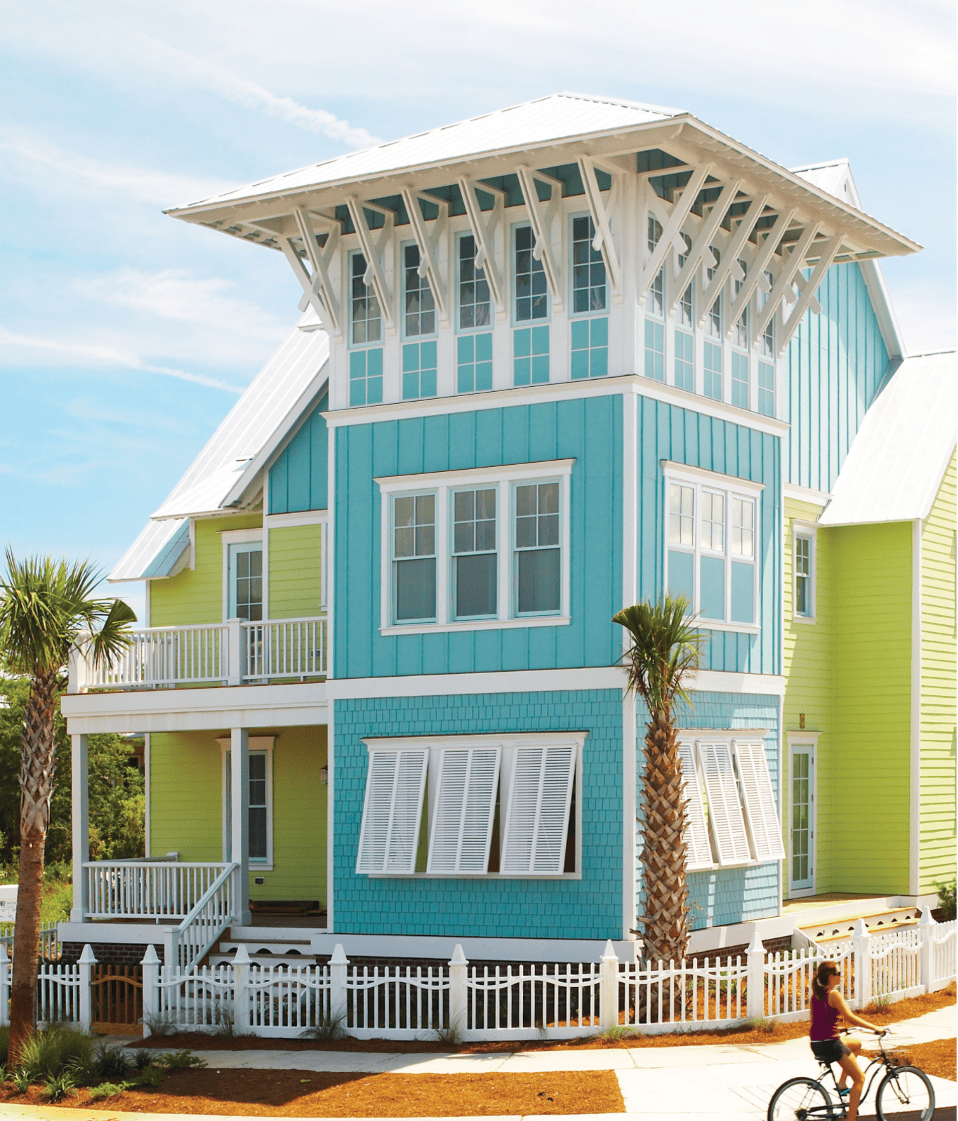 Colorful turquoise and lime beach house with white trim and balconies under a bright sky.