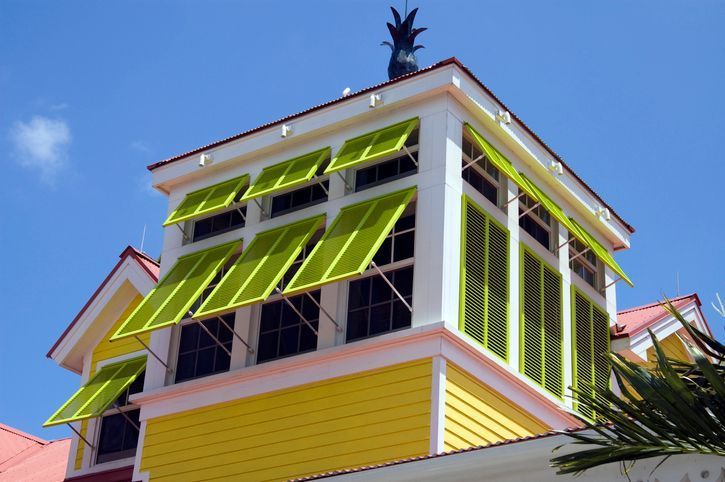 Bright yellow house with green shutters against a blue sky.