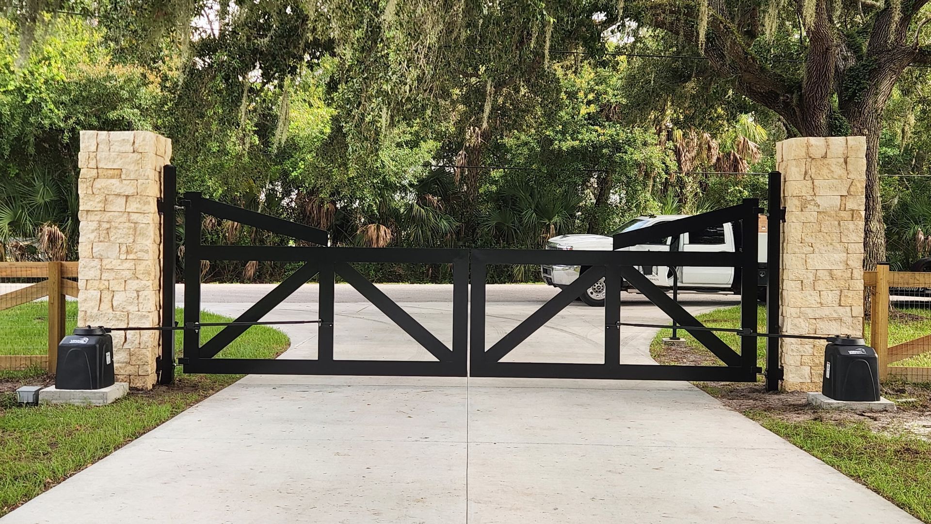 Black metal driveway gate between stone pillars at a landscaped home entrance
