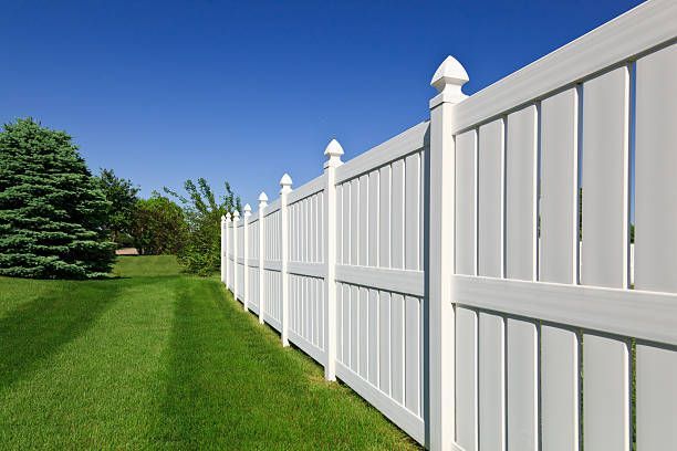 White vinyl fence in a green yard under a bright blue sky.