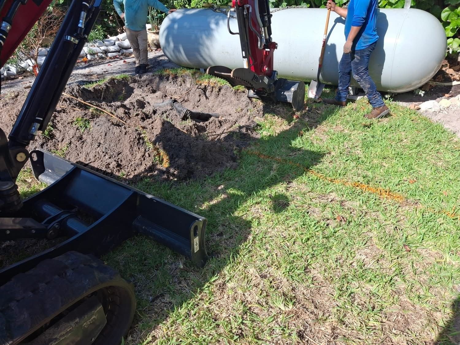 A man is digging a hole in the ground to install a propane tank.