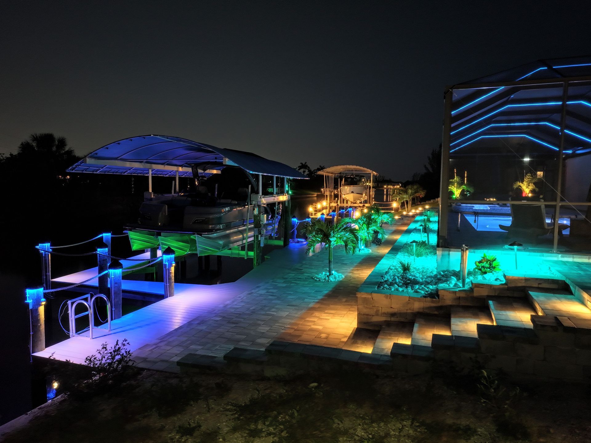 Nighttime view of a boat dock lit with vibrant blue and green LED lights.