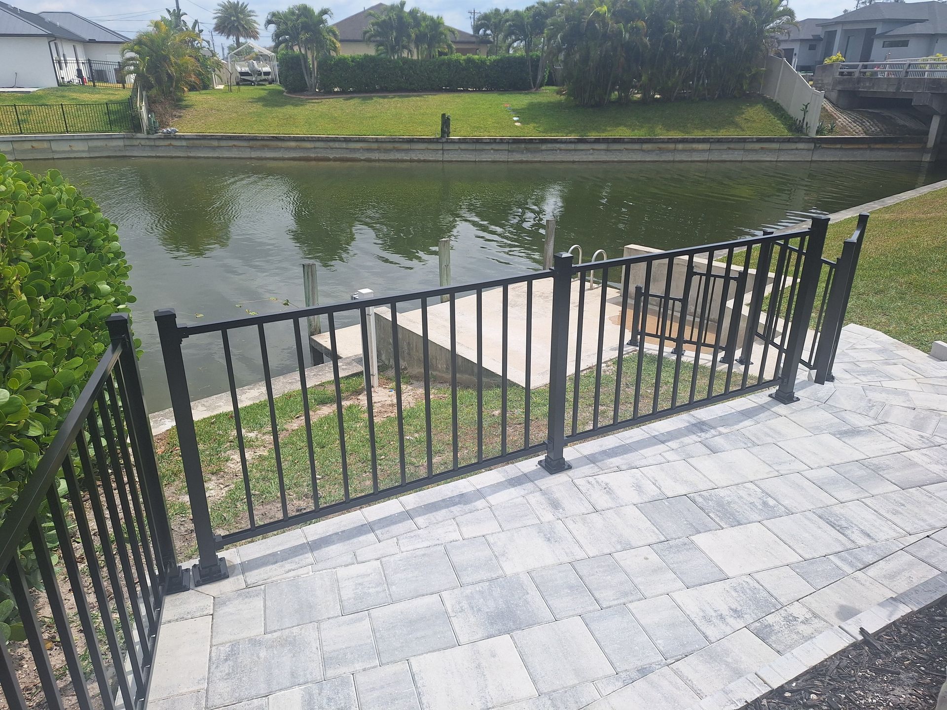 A black fence surrounds a patio overlooking a body of water.