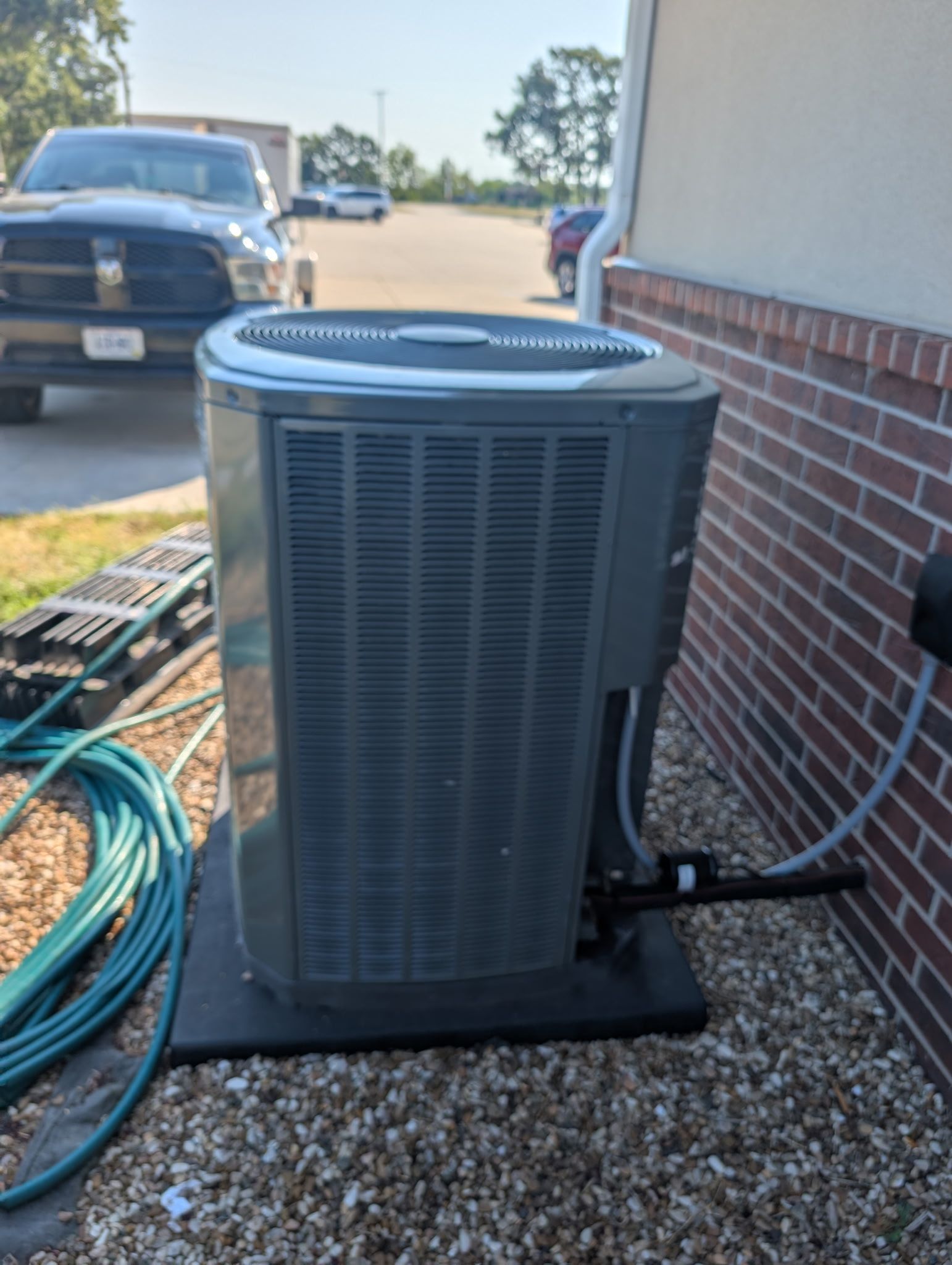 air conditioning unit next to brick wall, sitting on a black pad, with a truck in the background