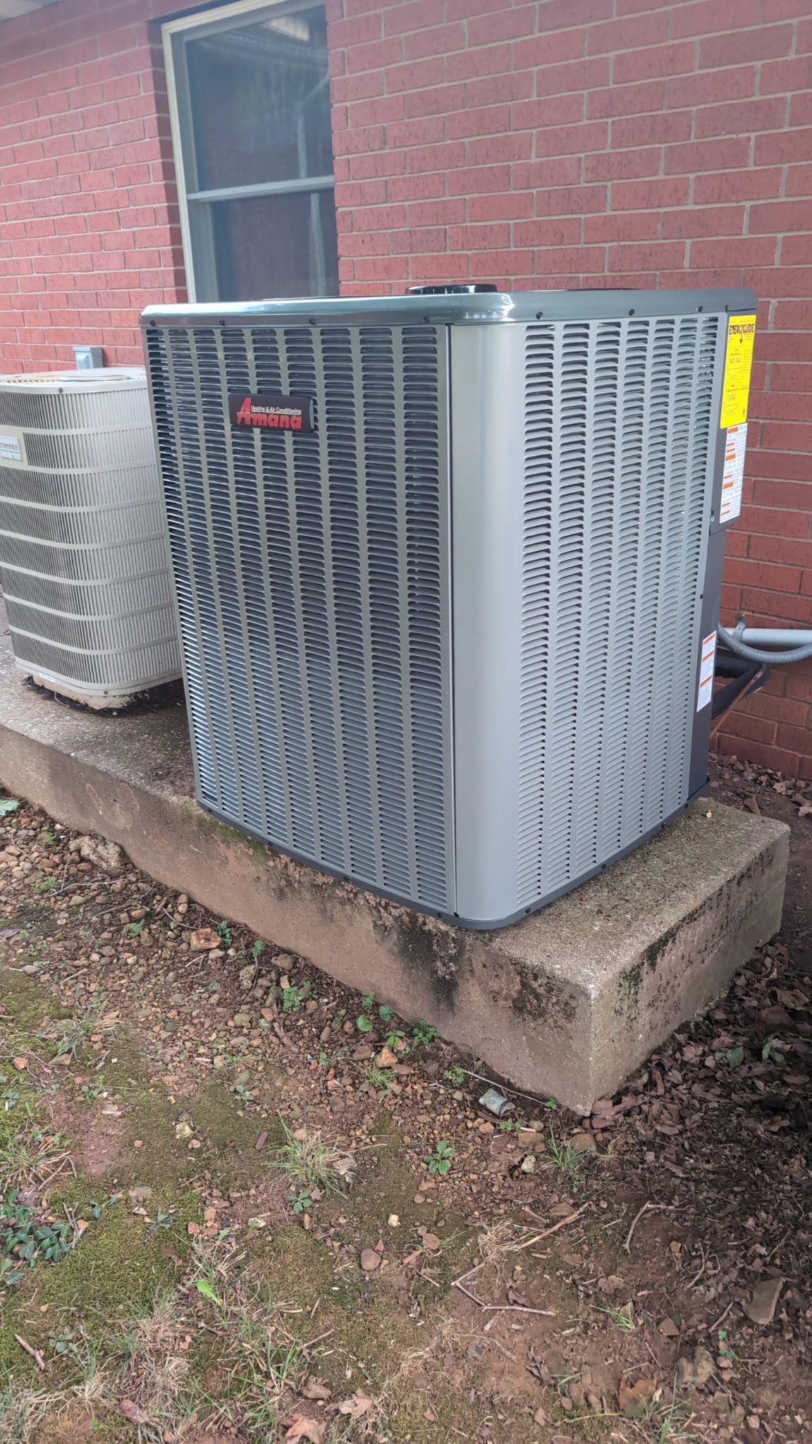 a new outdoor air conditioning unit on a concrete base, near a brick wall