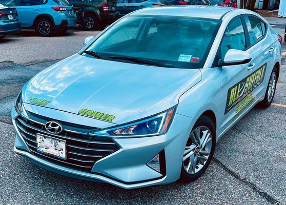 Light blue Hyundai Elantra with driving school signs parked outdoors.