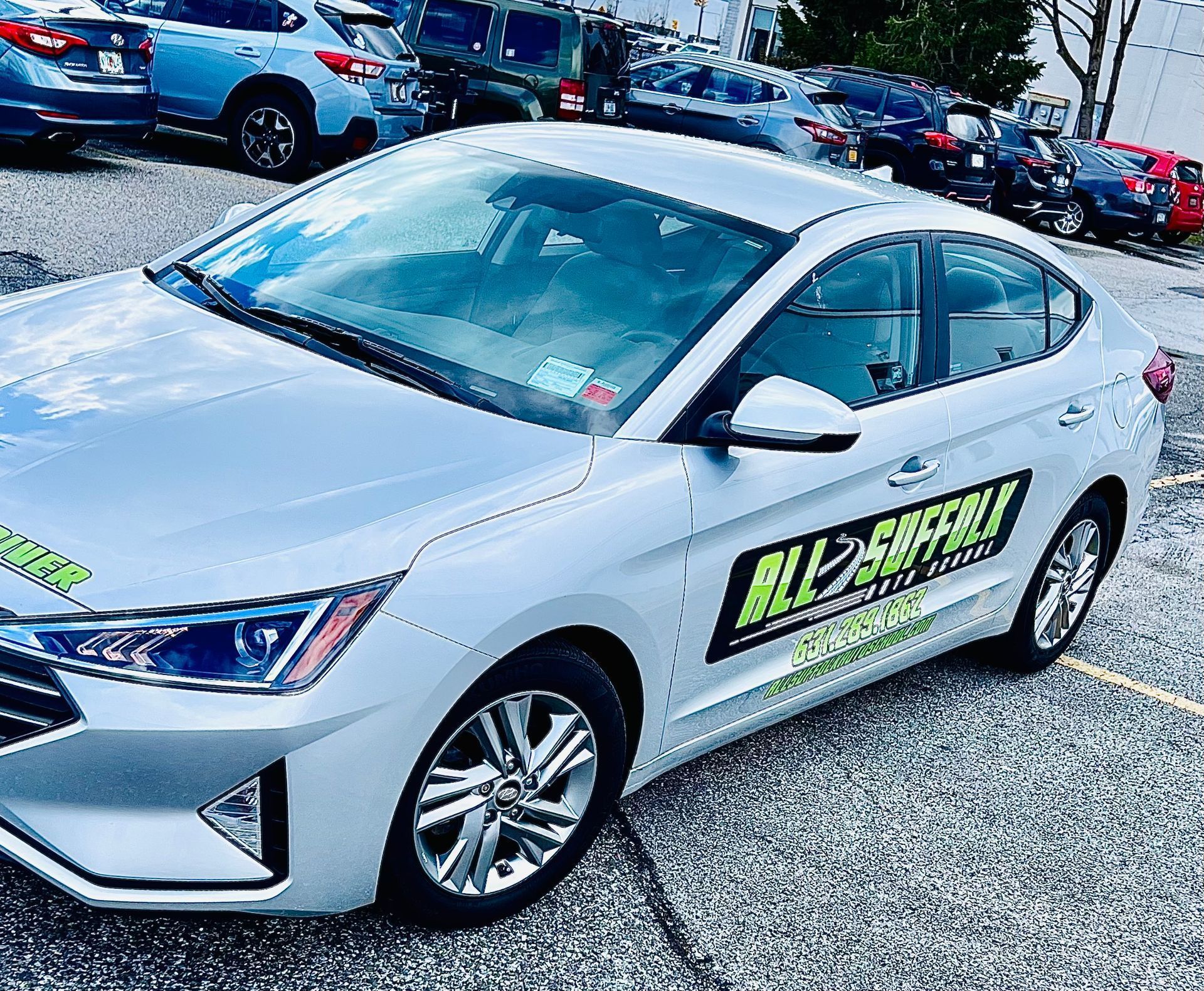 Silver sedan with driving school logo, parked in a lot.