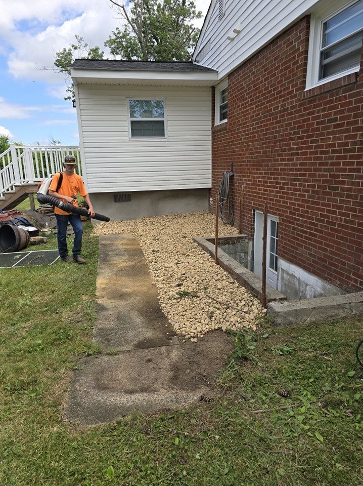 A man is standing in front of a brick house holding a blower.