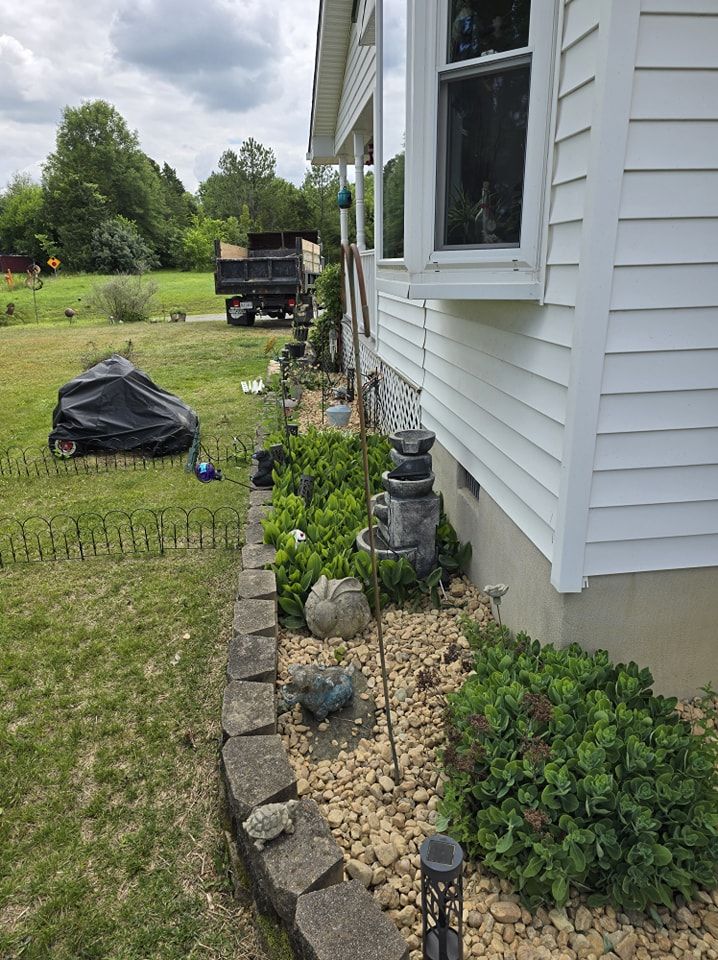 A white house with a lot of plants and rocks in front of it.