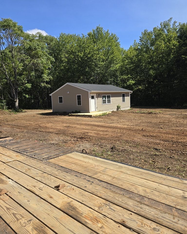 A small house is sitting in the middle of a dirt field surrounded by trees.