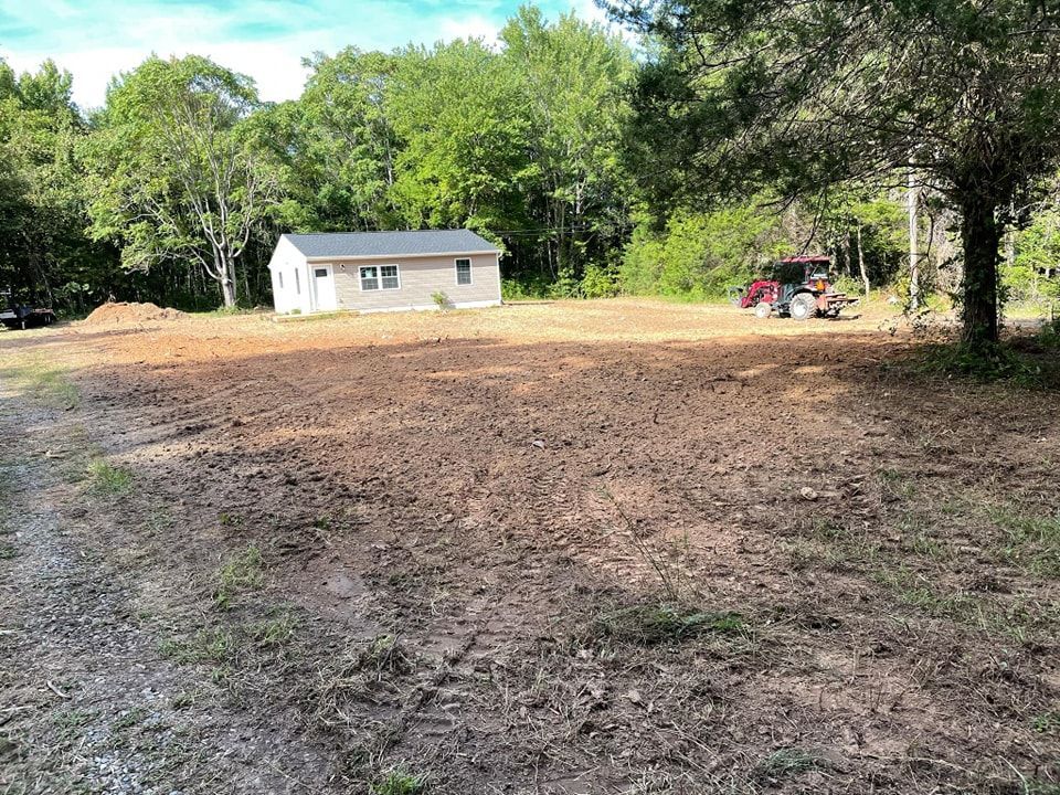 A house is sitting in the middle of a dirt field surrounded by trees.