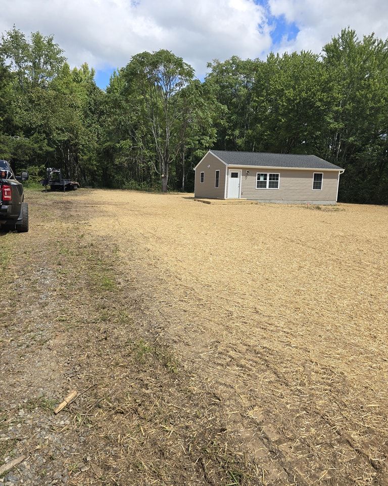 A house is sitting in the middle of a dirt field surrounded by trees.