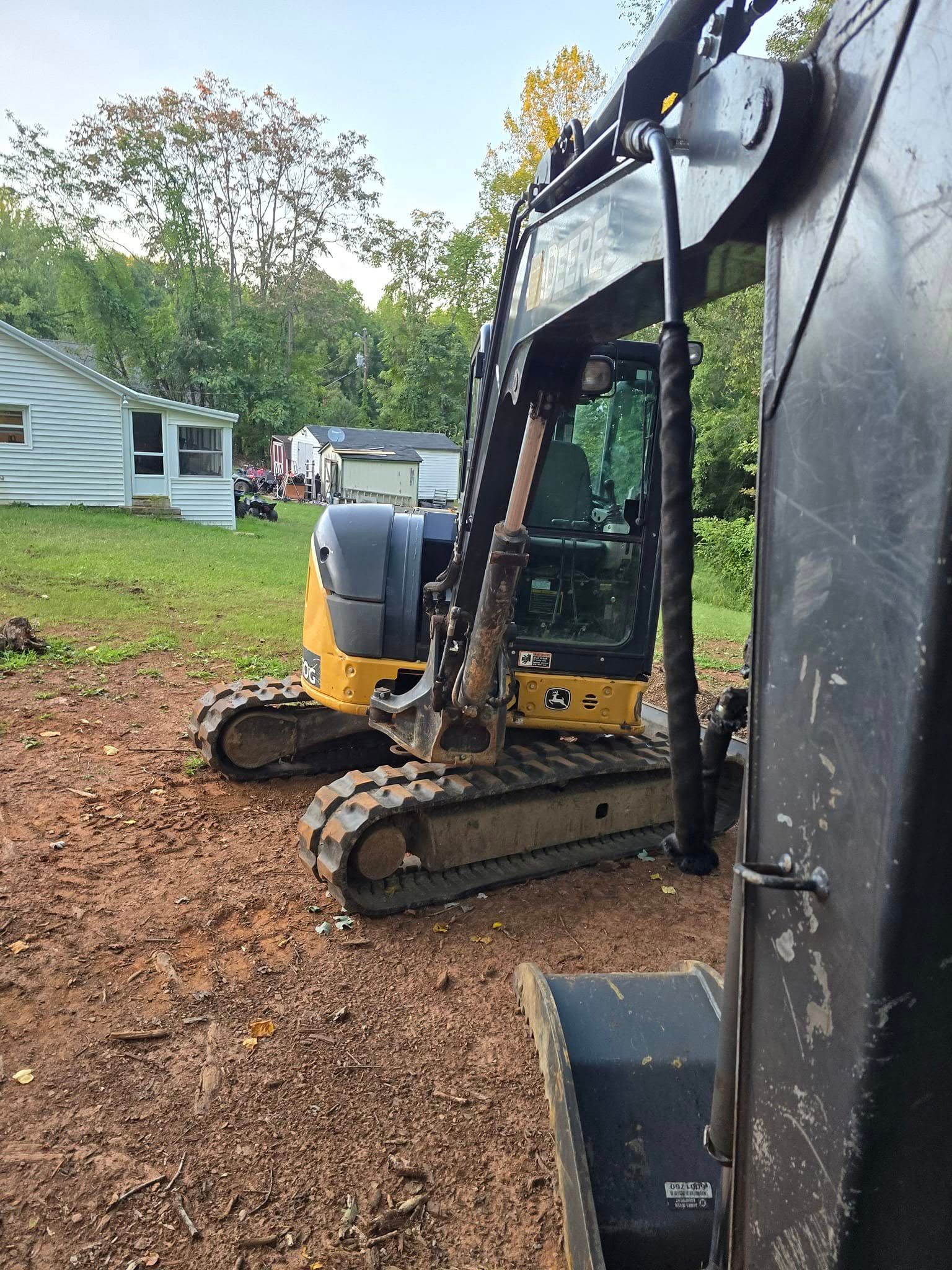 A yellow excavator is parked in a dirt field in front of a house.