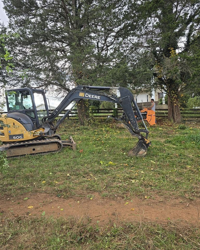 A small excavator is sitting in the middle of a grassy field.