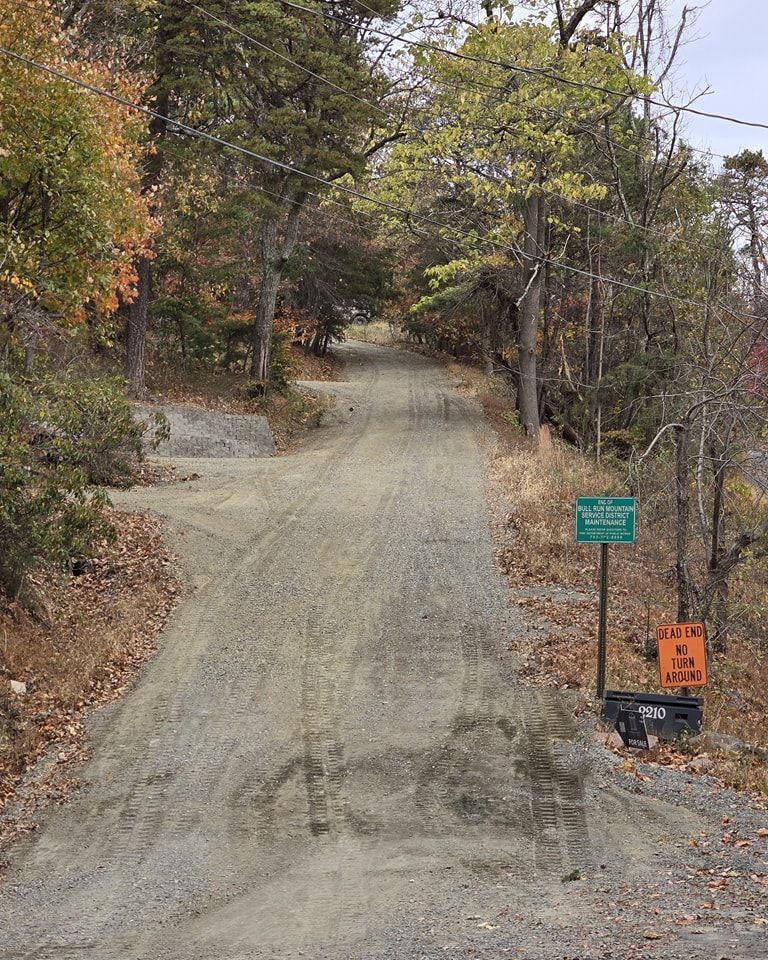 A dirt road going through a forest with trees on both sides.