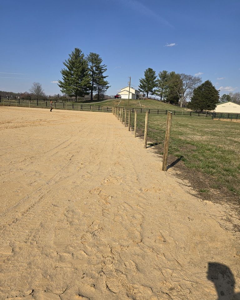 A dirt path leading to a fenced in area with trees in the background.