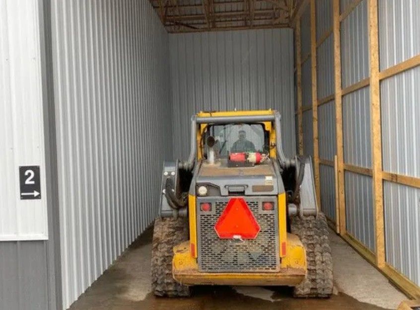 A yellow skid steer loader sits inside a metal storage unit labeled with the number 2.