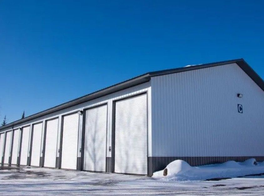 A row of white, metal-sided storage units under a clear blue sky, with snow on the ground in front of the building.