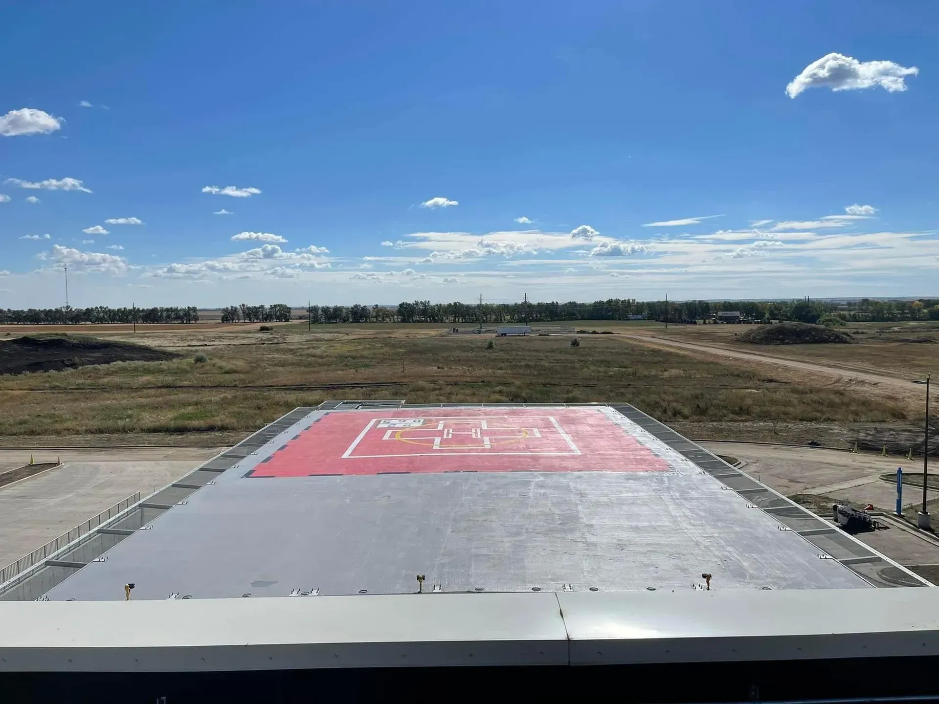 An elevated helipad with a red landing zone marker, set against a vast, open landscape under a clear blue sky.