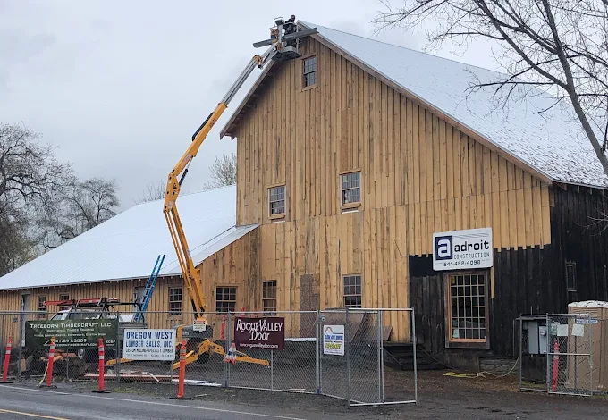A yellow construction lift is reaching towards a wooden building. Snow covers the roof.