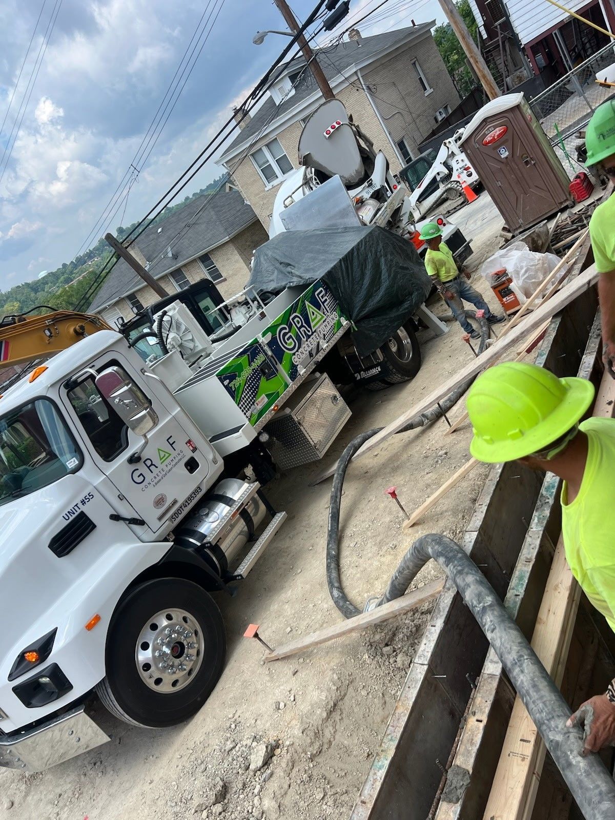 Construction site: concrete truck pouring concrete into a wooden frame, workers in safety vests.