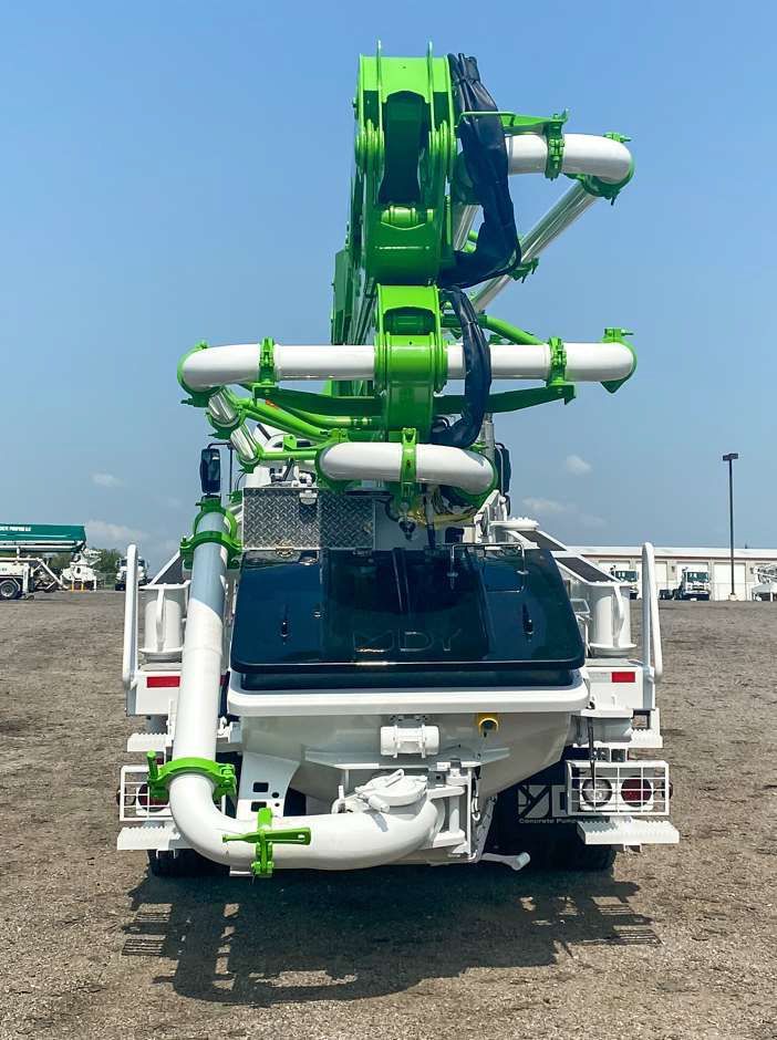 A green and white concrete pump truck is parked in a dirt field.