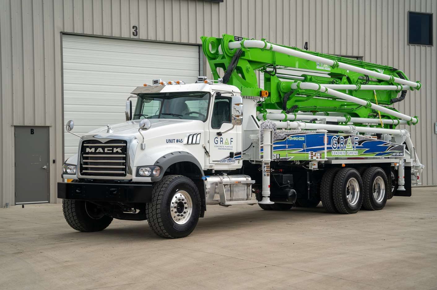A white and green concrete pump truck is parked in front of a building.