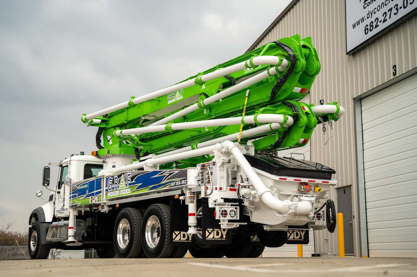 A green and white concrete pump truck is parked in front of a building.