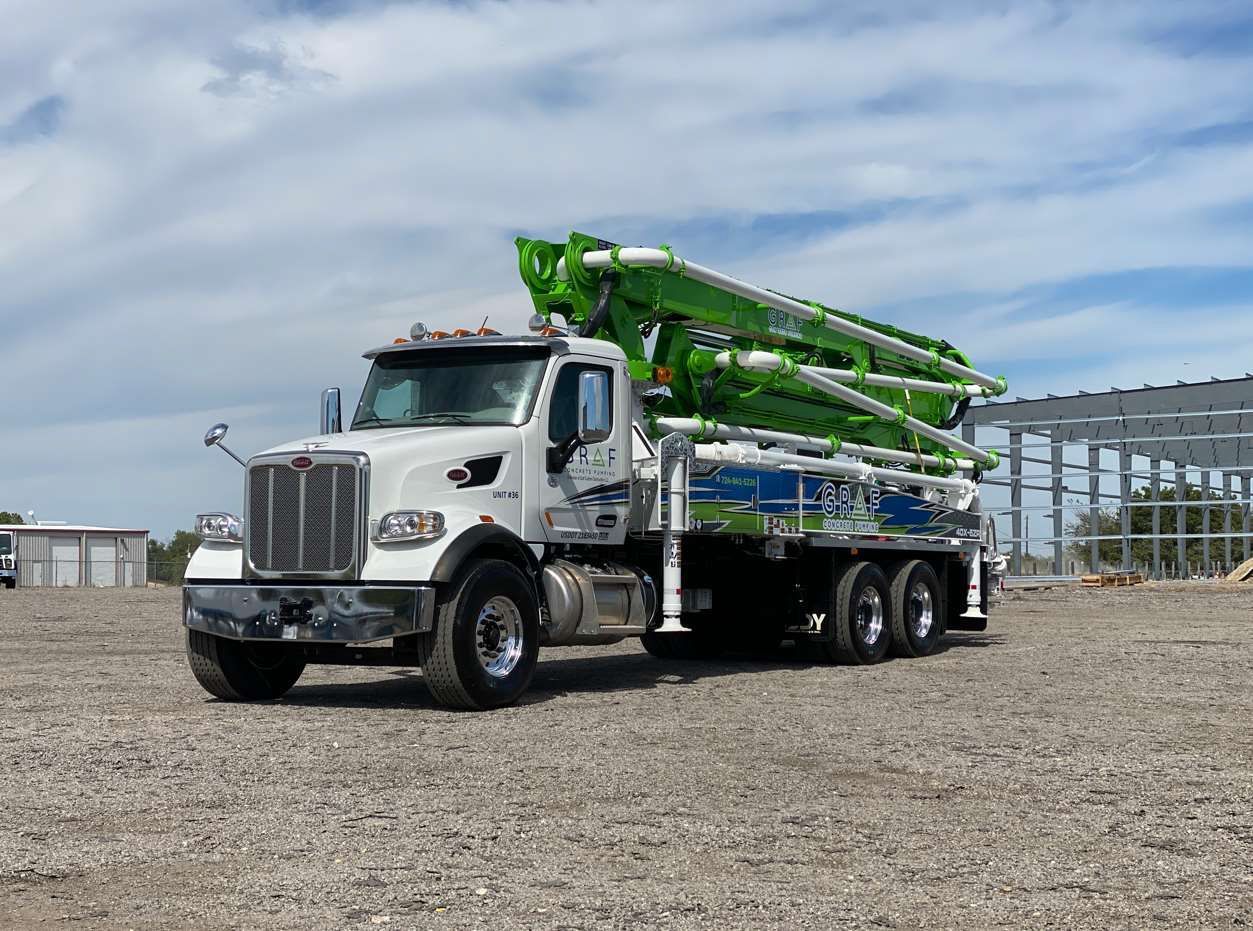 A white and green concrete pump truck is parked in a gravel lot.