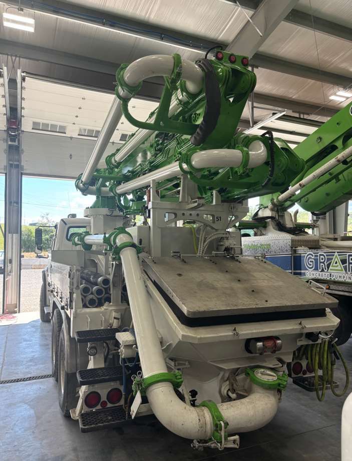 A green and white concrete pump truck is parked in a garage.