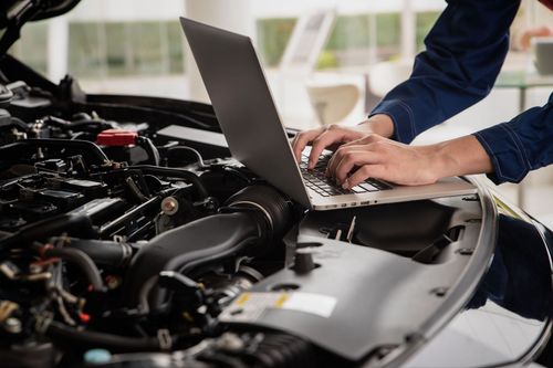 Mechanic using a laptop beside an open car engine in a garage