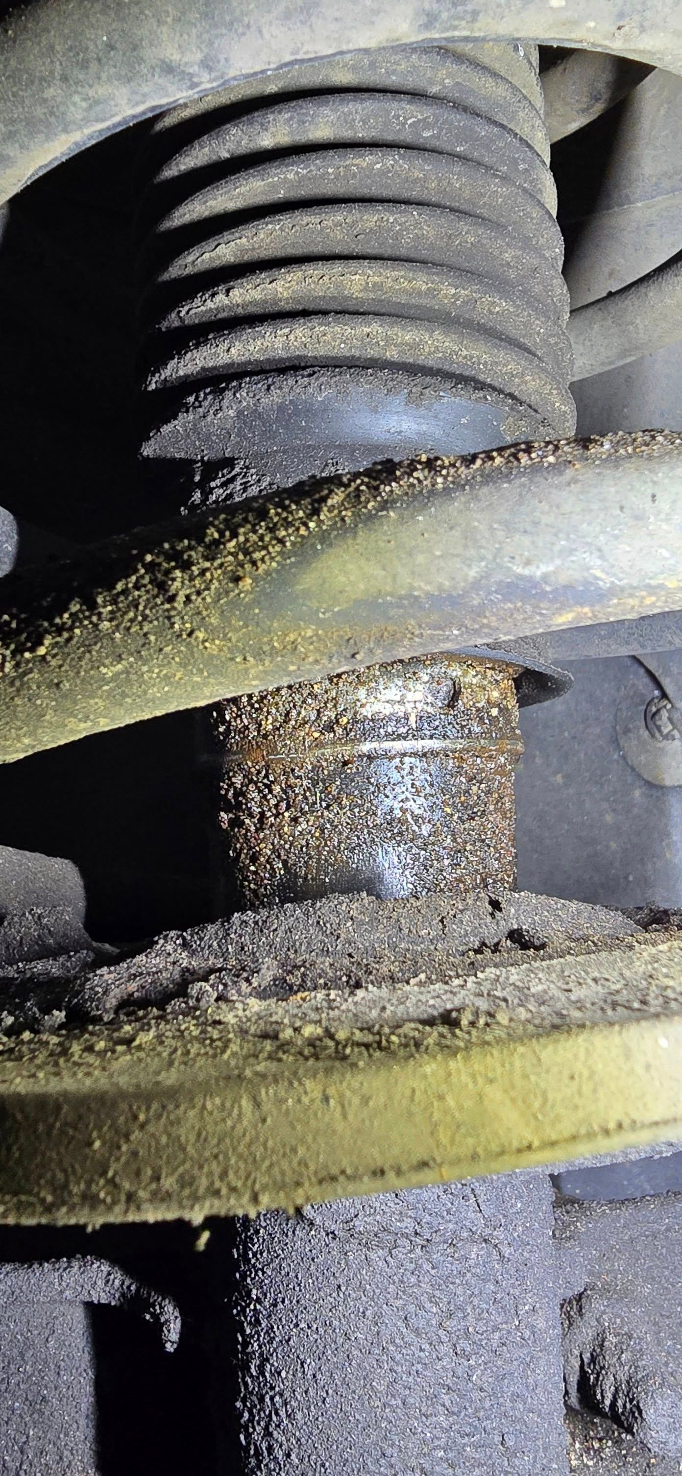 Close-up of a dirty metal suspension spring with dust and rust buildup.