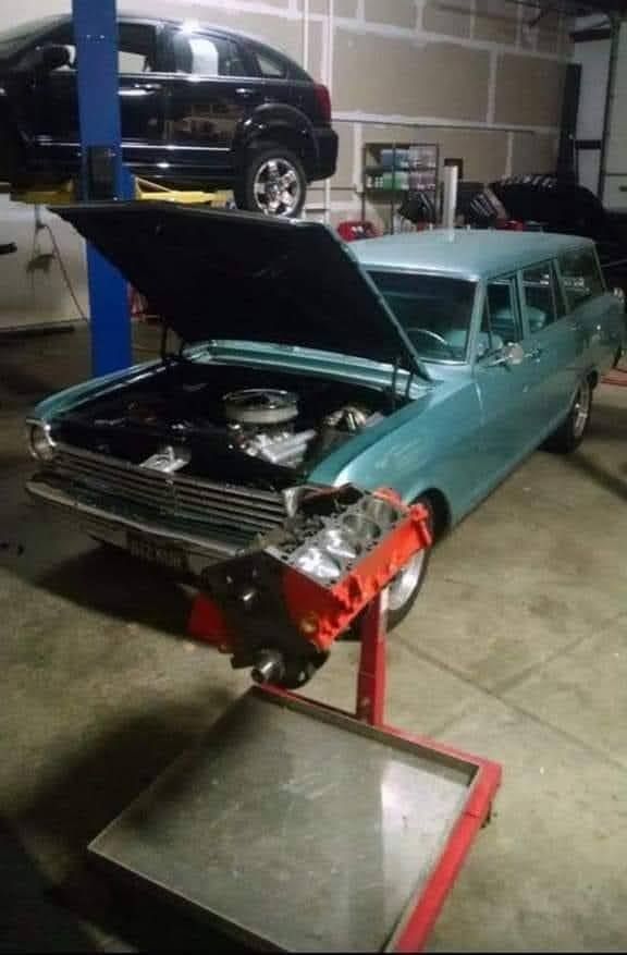 Classic teal car with hood open in a garage, showing engine work on a lift.