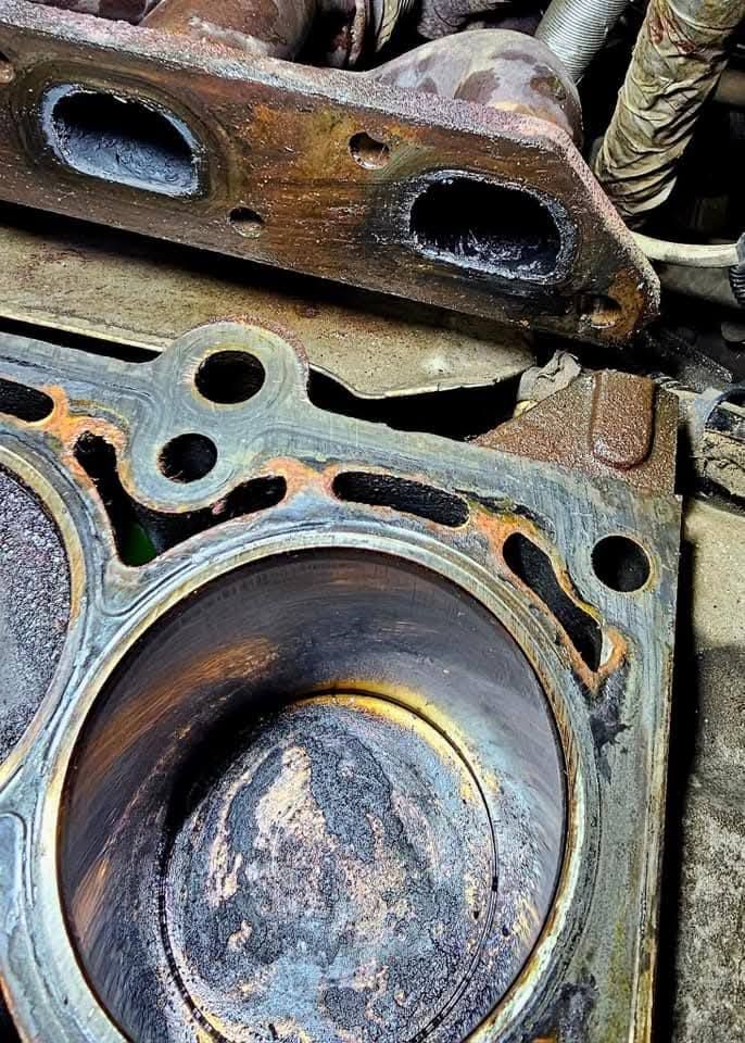 Rusty engine cylinder head and piston close-up with gasket damage and corrosion