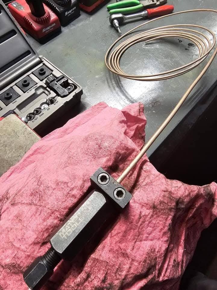 Coiled copper tubing and a small metal tool on a pink rag at a workbench, with pliers nearby