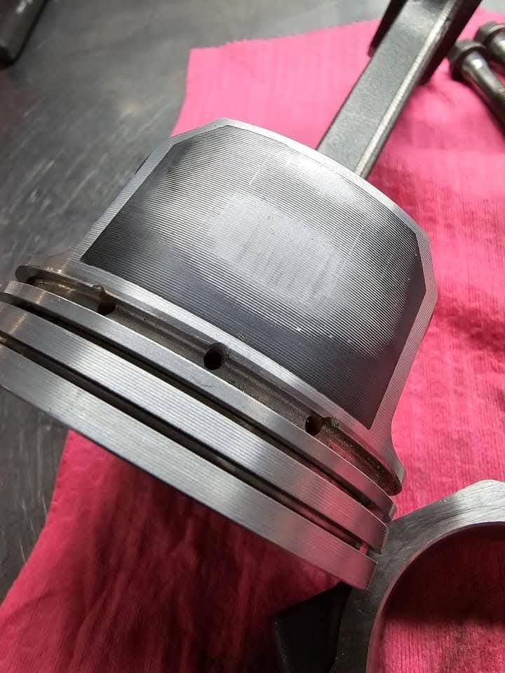 Close-up of a metal piston with grooves and rings on a pink cloth.