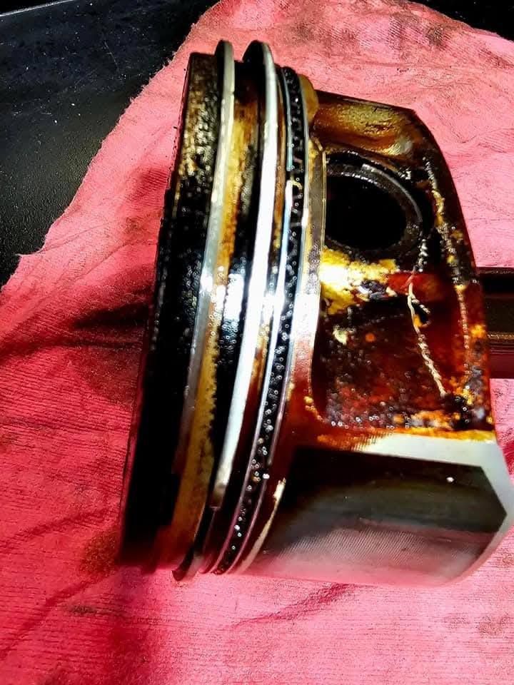 Close-up of a damaged piston with carbon buildup on a red cloth background