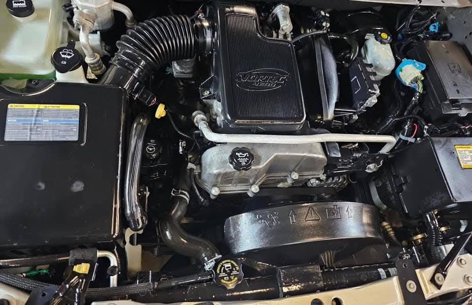 Car engine bay with black plastic covers, hoses, and silver metal components.