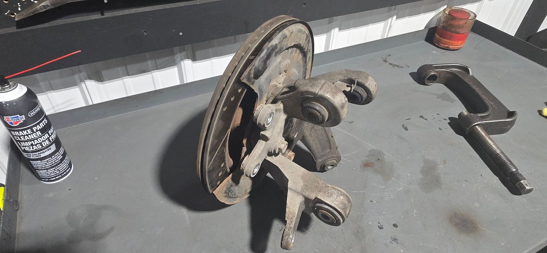 Car wheel hub and brake rotor on a workbench with hand tools and spray cans nearby