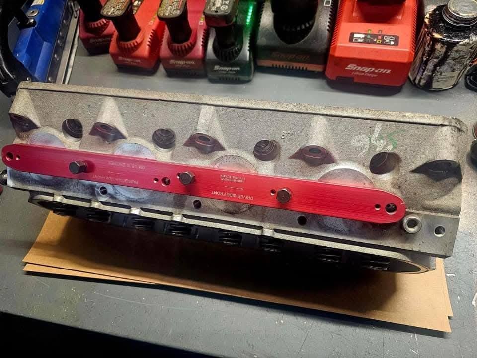 Red anodized engine part with several ports, resting on a workbench in a garage.
