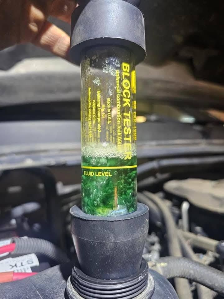 Car coolant reservoir with green fluid level visible through a clear tube under the hood