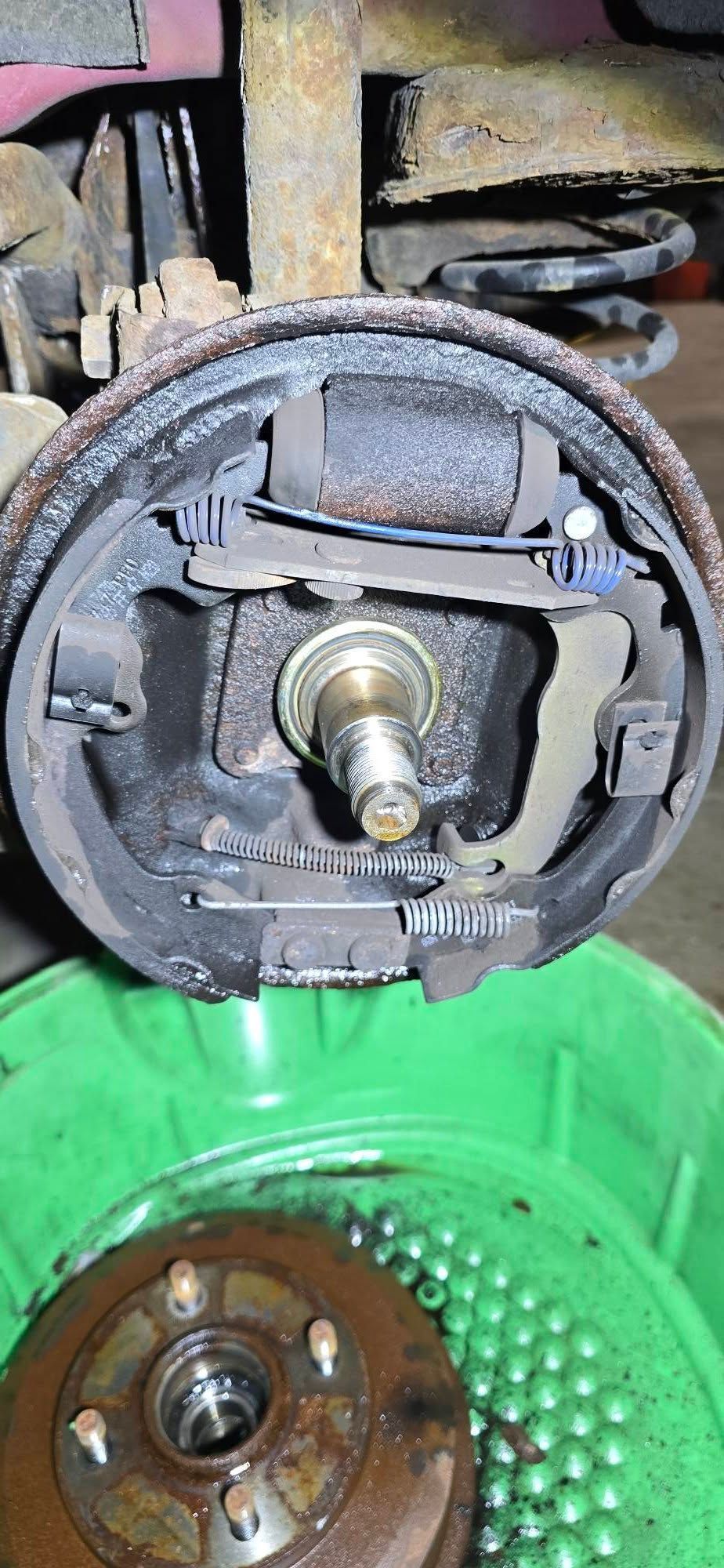 Close-up of a disassembled brake assembly with rusted parts and a green container below.