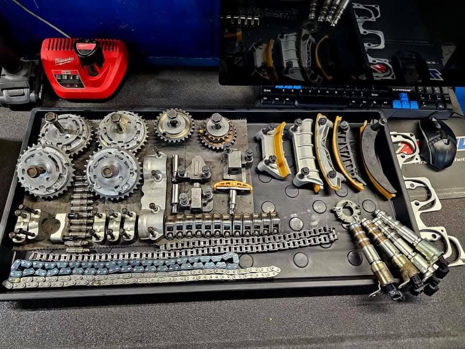 Assorted mechanical gears, chains, and metal parts laid out on a workbench for repair or assembly