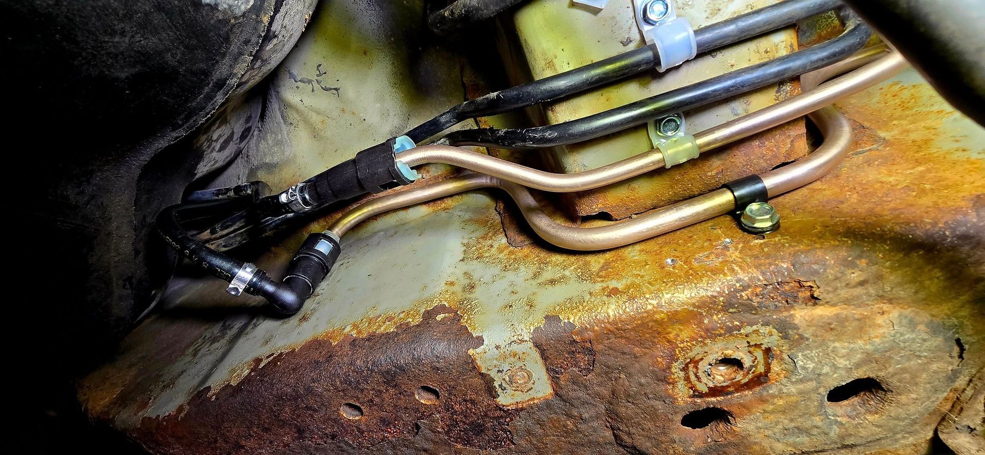 Rusty metal pipes and hoses connected to a corroded machine surface with grime and discoloration.